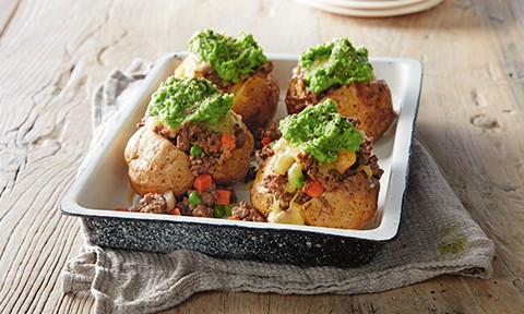 Baked potatoes in a dish topped with savoury mince and peas