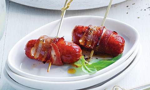 Two bacon-wrapped chorizo garnished with basil leaves.