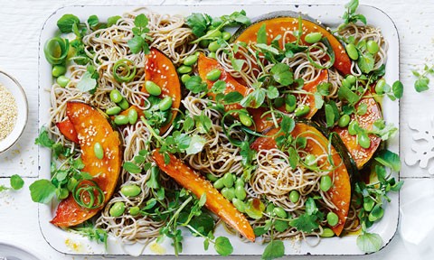 Teriyaki roasted pumpkin and noodle salad on a serving dish, garnished with spring onion curls and toasted sesame seeds.
