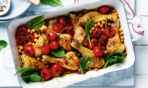 Chicken drumsticks and chickpea tray bake with roasted tomatoes and spinach leaves