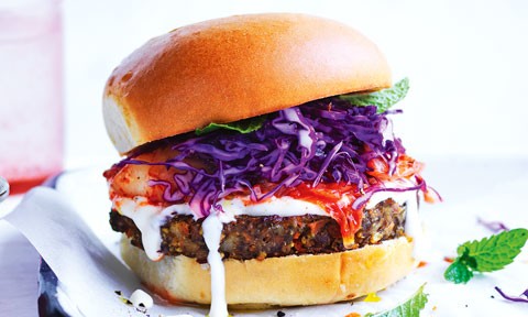 Close up of veggie and kimchi burger with purple cabbage and mayo garnished with mint.
