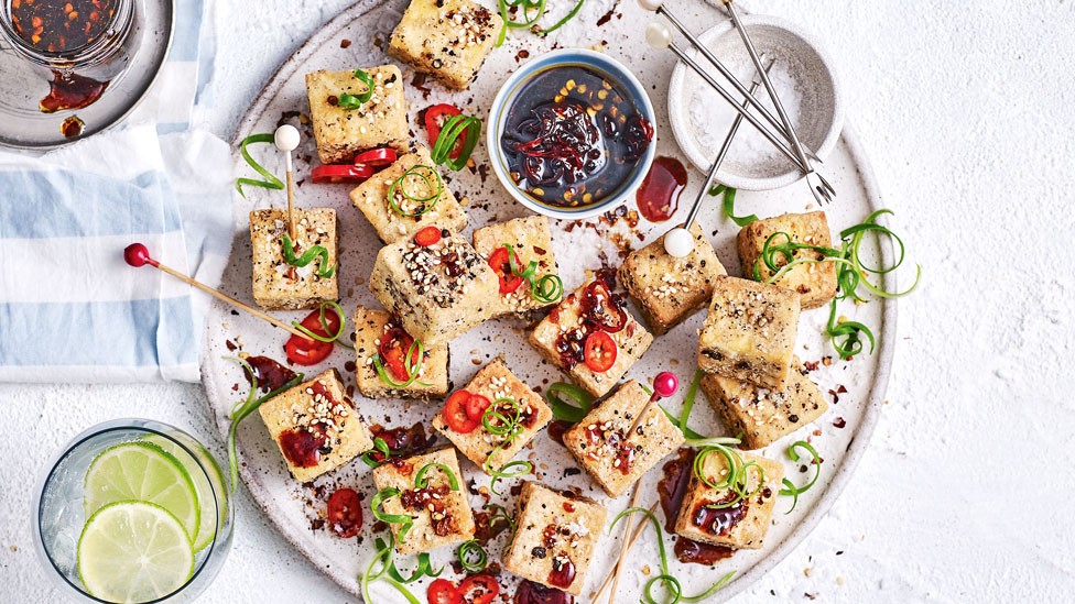 Platter of gluten free salt and pepper tofu squares, dressed in thinly sliced red chilli, spring onion curls and toasted sesame seeds.