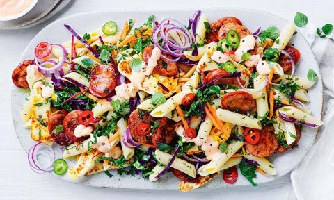 A serving platter of chorizo and pasta salad with red onion and parsley on top