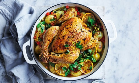 A roast chicken in a baking pot with lemon and parsley
