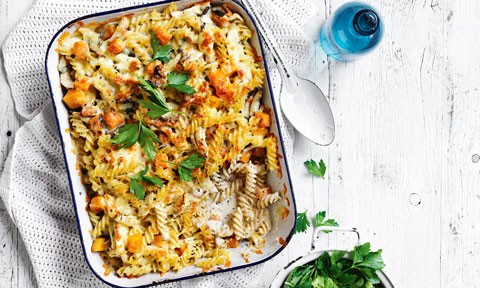 Chicken and mushroom pasta bake in a baking tray with parsley garnish and a serving spoon on the side