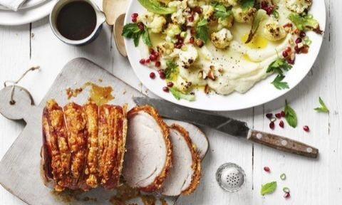 Curtis Stone's Roast Pork on a wooden board with Cauliflower Salad served with mash potato and garnished with pomegranate, cashew nuts, mint and parsley leaves. Gravy to the side.