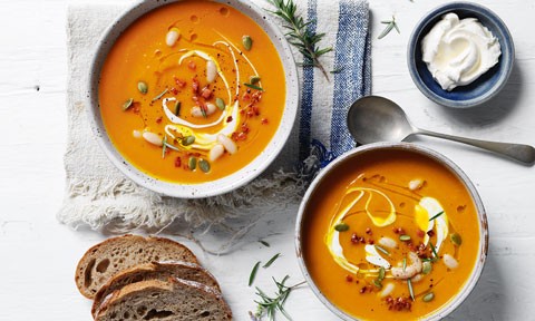 Two bowls of pumpkin and cannellini beans soup served with cream and pepitas on top
