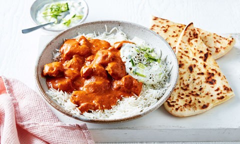 Butter chicken served on top of rice with raita and naan bread on the side