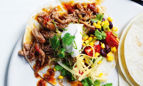 Pulled pork in a taco shell with corn salsa, cheese, sour cream and coriander