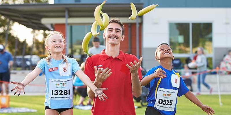 Coles team member throwing bananas with little athletics kids