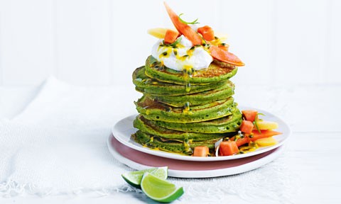 A stack of green pancakes topped with mango, papaya, and passionfruit