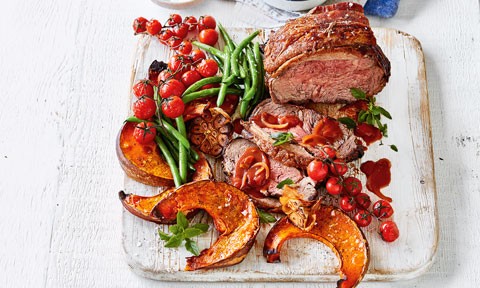  Roast Beef with Tomato and Red Wine Gravy on a wooden board. Served with tomato on the vine and pumpkin.