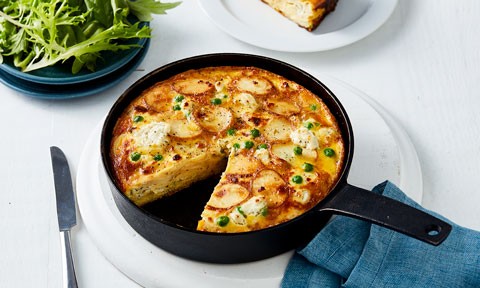 Potato and Pea Frittata in a pan, with a wedge cut out and a side of salad
