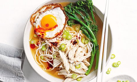 A bowl of soup with noodles, chicken, greens and a fried egg