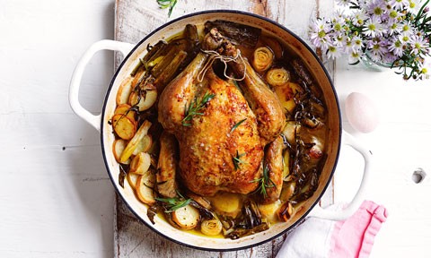 Roast chicken served in a casserole dish with leeks and rosemary sprigs 