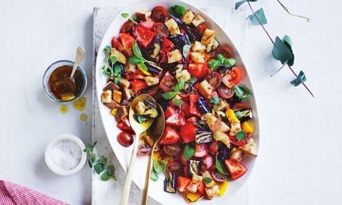 Tomato, bread and eggplant salad served in a large plate topped with basil leaves with vinaigrette on the side
