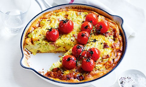 Whole bacon and leek frittata with roasted vine tomatoes on top and a slice cut out