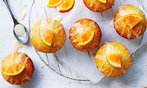 Five orange muffins with icing and sliced orange on top