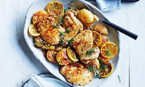 Baked lemon rosemary chicken served on a serving platter with grilled lemon and herbs