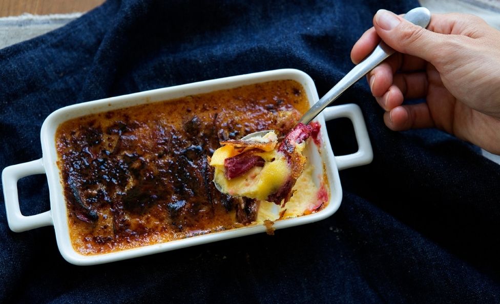 Someone taking a spoon out of a rhubarb creme brulee