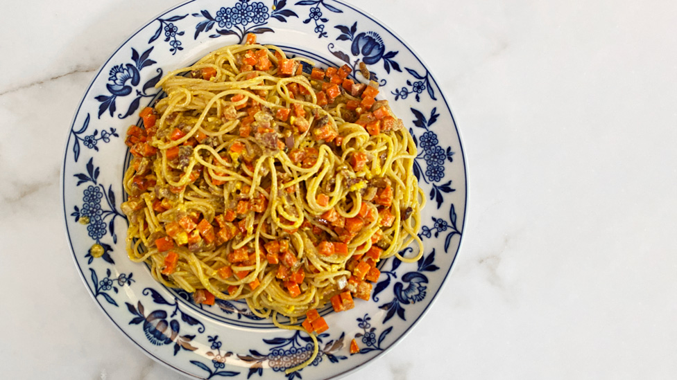 A creamy spaghetti carbonara with chopped carrot cubes.