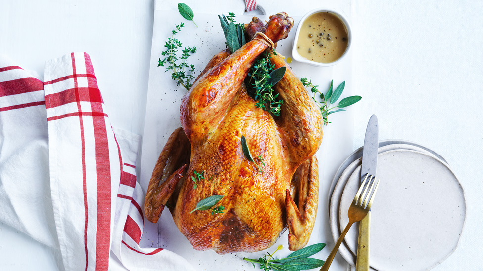 A tray with golden roast turkey sprinkled with fresh herbs, accompanied by a ramekin of peppercorn mustard gravy.