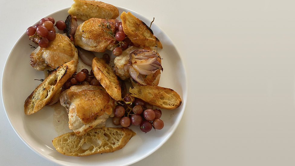 A plate of roast chicken, bread, onion and grapes.