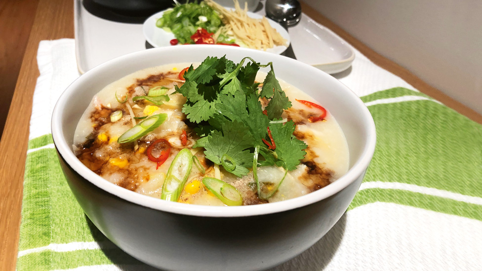 A bowl of chicken, sweet corn and rice soup topped with green onions and coriander.