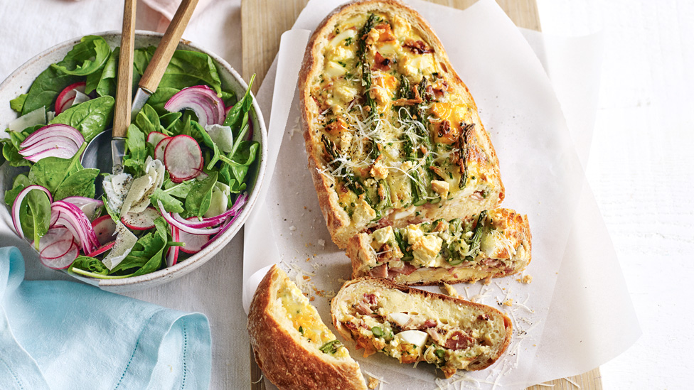 An egg and bacon loaded loaf with shaved parmesan and a side salad.