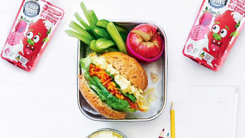 An egg and salad roll in a lunch box with an apple and celery