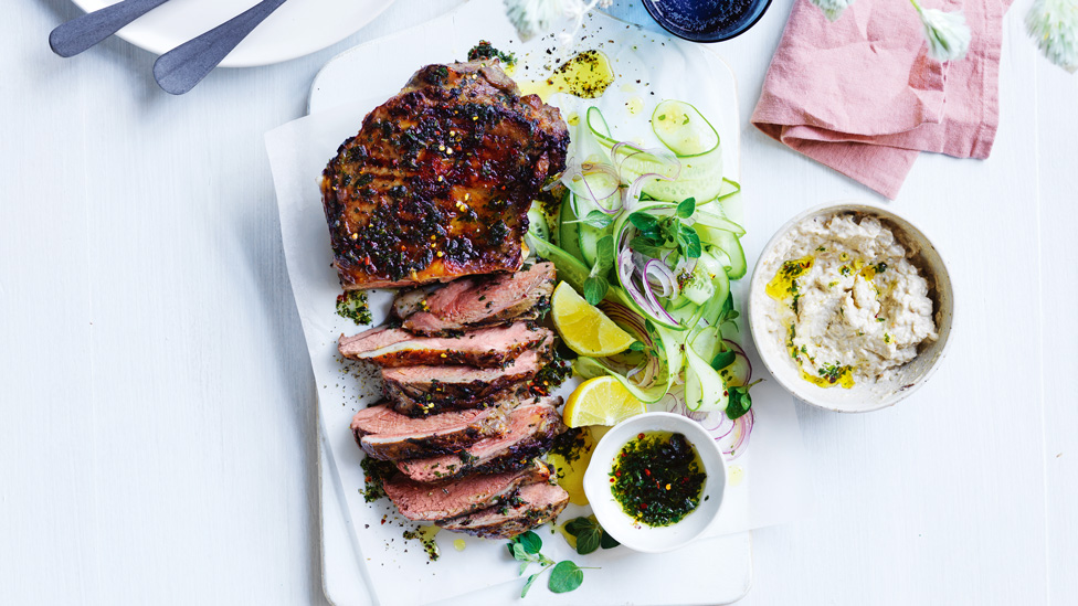 Sliced lamb served next to spring greens with lime wedges and onion relish