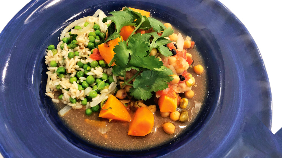 A bowl of hot pot packed with chick peas, rice, and veggies like sweet potato and peas.