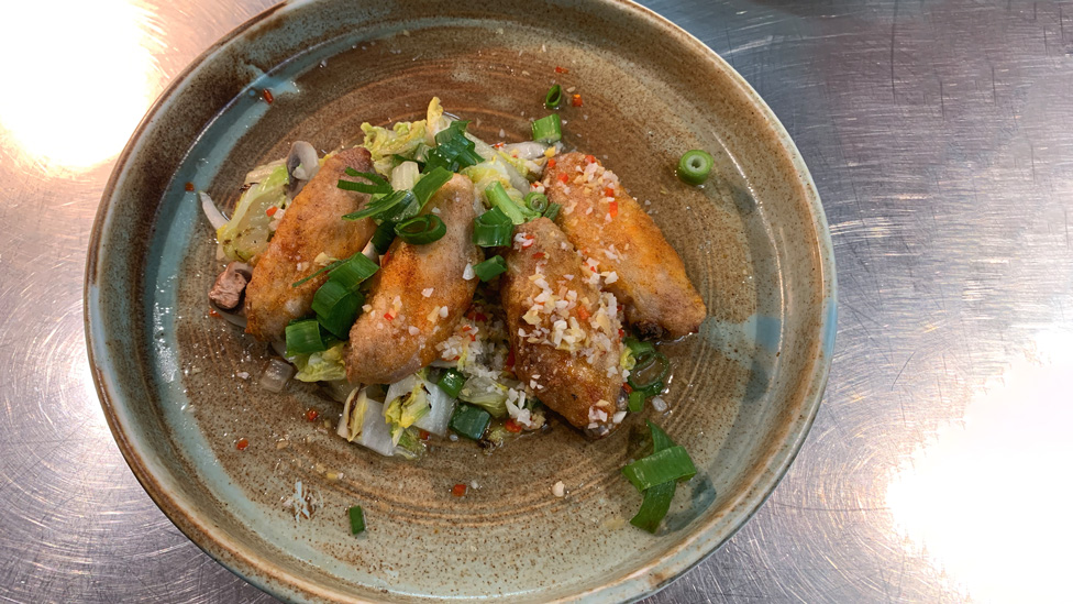 A bowl of four chicken wings topped with spring onions, ginger, garlic and chilli.