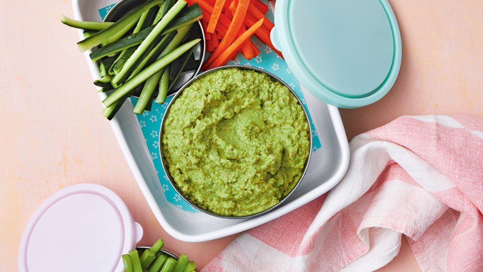 Pea hommus served in a bowl with cucumber and carrot sticks