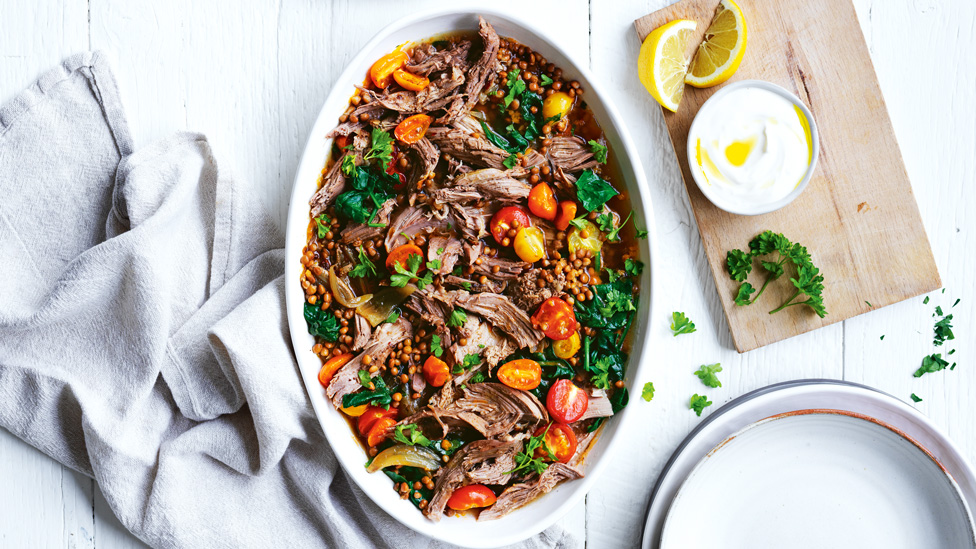 Pulled lamb and lentils in a casserole dish served with tomatoes, parsley and lemon wedges