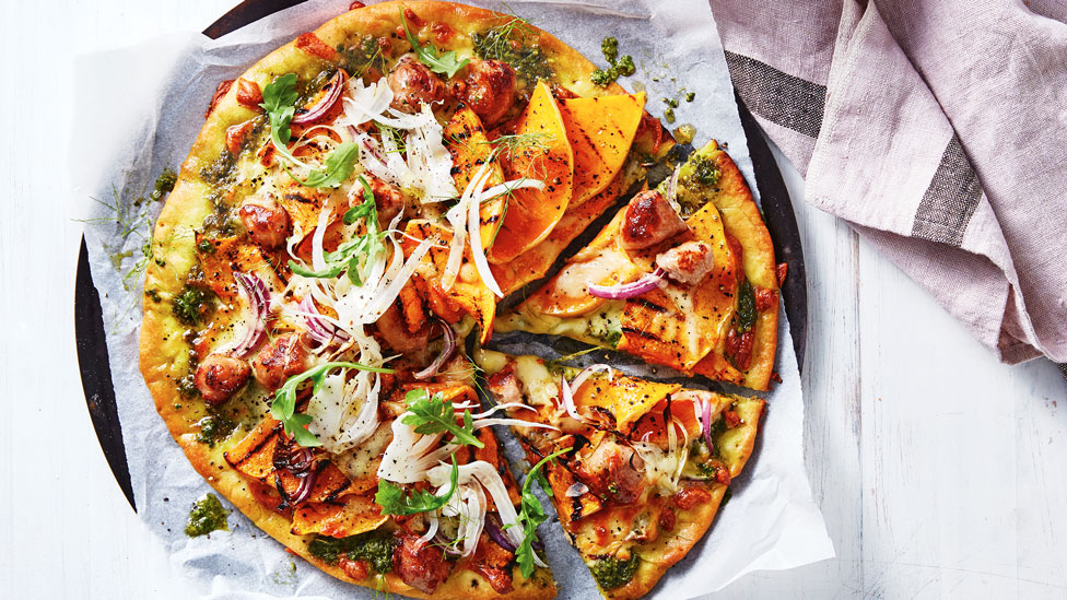 Pumpkin, Sausage and Rocket Pesto Pizza on baking paper, next to a lavendar towel