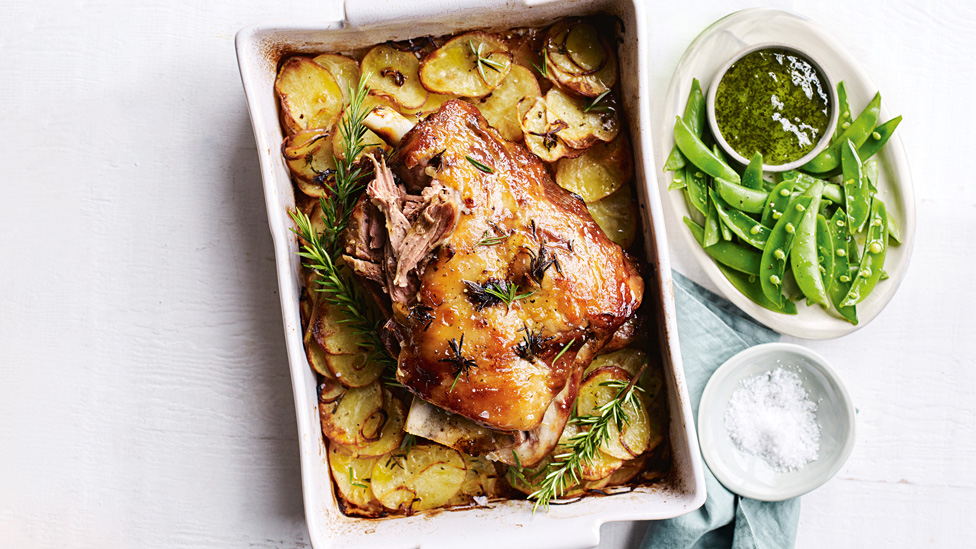 Roast Lamb with Mint Jelly Glaze garnished with rosemary. Laying on thinly slived roast potatoes in the oven dish.