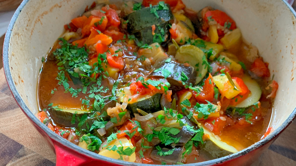 A pot of soft vegetables in a rich saucy and topped with chopped herbs.
