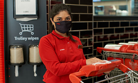 Coles employee wiping handle bars of a Coles trolley