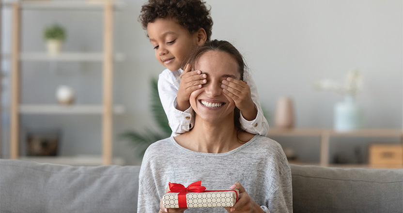 child covering eyes of mother holding gift
