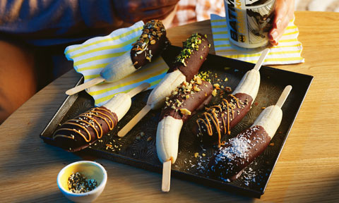 A tray of chocolate-dipped bananas drizzled with peanut butter and chopped nuts.
