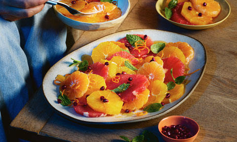 A colourful plate of sliced citrus fruits with mint and pomegranate jewels.