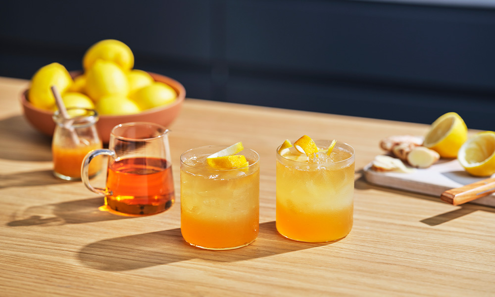 honey lemon whisky cocktails on a wooden table with lemons in the background