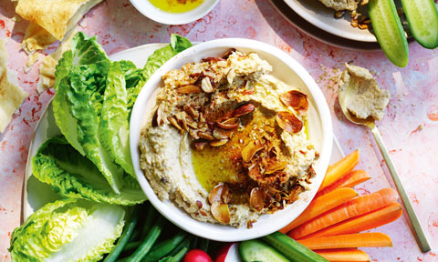 Roast cauliflower hommus in a bowl with vegetable sticks around it on a plate