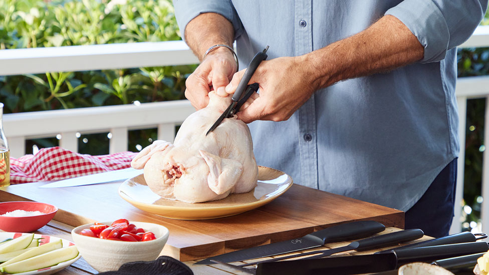 raw whole chicken being cut with scissors