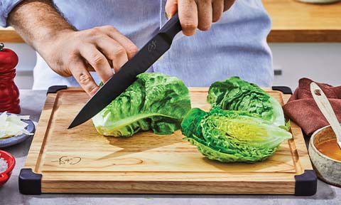 Cos lettuce being halved on a chopping board.