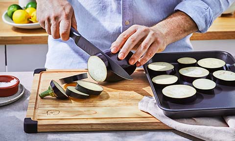 Eggplant being sliced on a chopping board.
