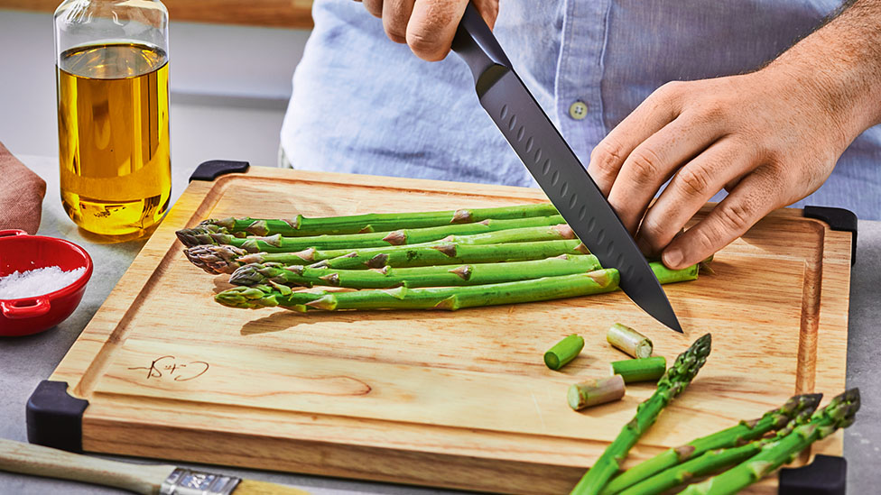 Asparagus on a chopping board, ends being cut off