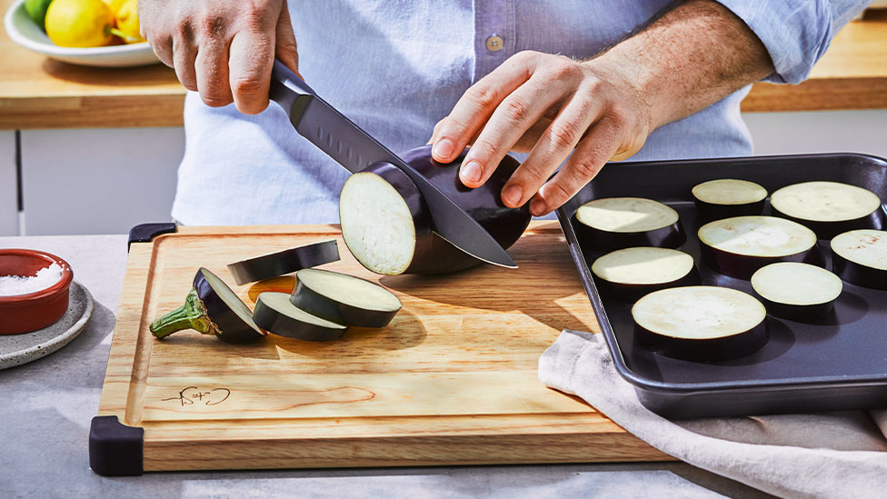 Eggplant being sliced on chopping board.