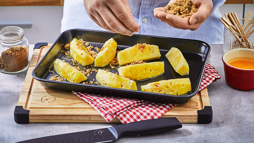 Pineapple in a baking tray being sprinkled with sugar.